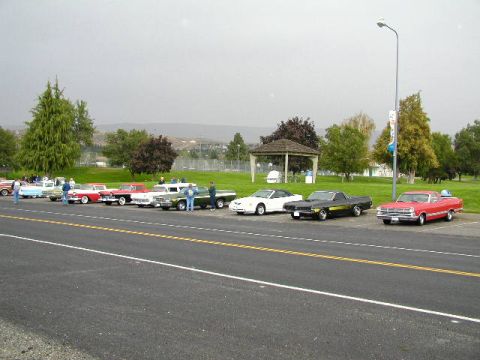 1967 Ford Ranchero - Several classic cars are parked in a line next to a road on a cloudy day.