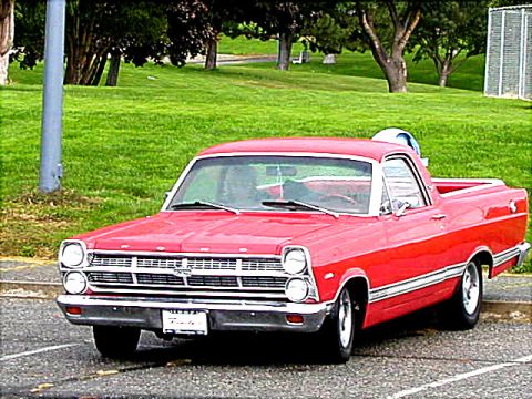 1967 Ford Ranchero - This red Ford Ranchero is parked in a lot with a grassy area and trees behind it.