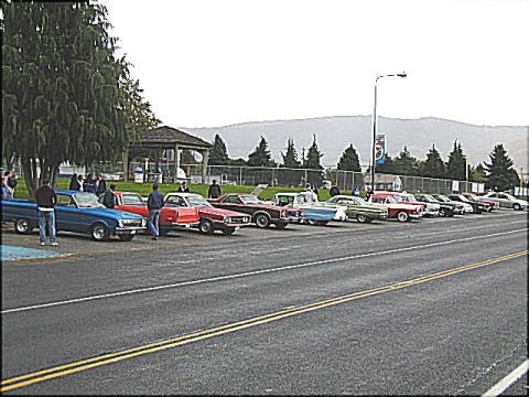 1967 Ford Ranchero - A gathering of vintage automobiles is parked in a lot, with a gazebo and trees in the background.