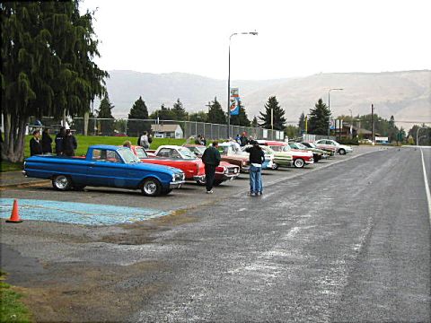 1967 Ford Ranchero - A line of vintage vehicles are parked in a lot under an overcast sky.