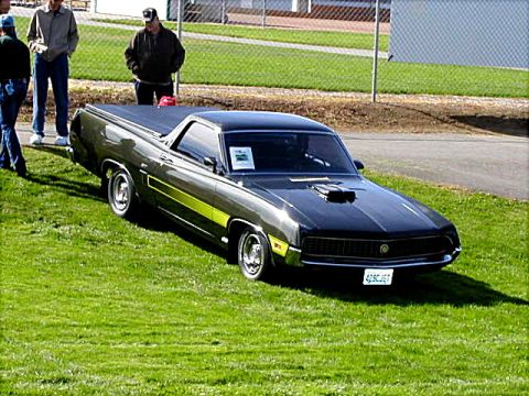 1967 Ford Ranchero - A dark green 1970 Ford Ranchero with a prominent hood scoop and yellow side stripe is displayed on a grassy area.