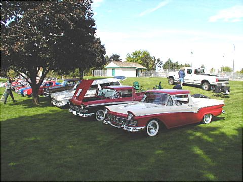 1967 Ford Ranchero - A red and white 1957 Ford Ranchero is displayed at an outdoor car show alongside other classic vehicles.