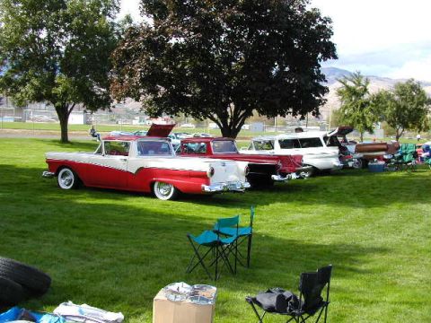 1967 Ford Ranchero - A red and white 1957 Ford Ranchero is parked on a grassy field with other vehicles and chairs.