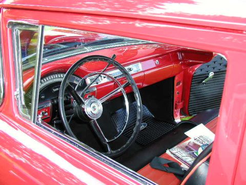 1967 Ford Ranchero - The interior of a red 1957 Ford Fairlane 500 shows its classic dashboard and steering wheel, with a magazine resting on the seat.