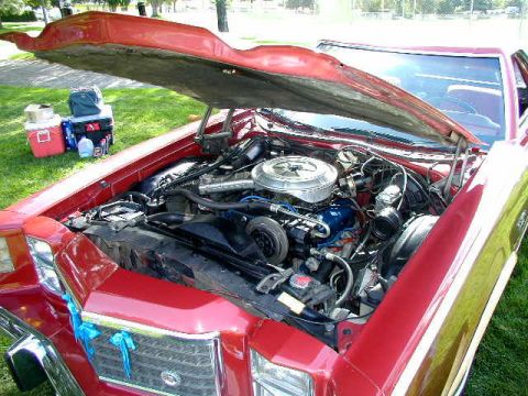 1967 Ford Ranchero - The engine bay of a red 1977 Ford Ranchero is visible with the hood up, revealing the V8 engine.