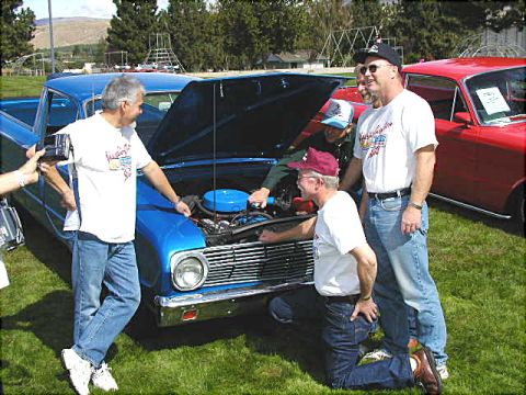 1967 Ford Ranchero - Men examine the engine of a blue 1963 Ford Ranchero at an outdoor event, with a red car nearby.