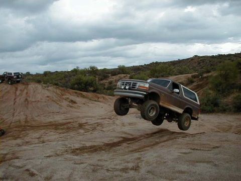 1993 Ford Bronco - A lifted Ford Bronco is airborne over a sandy terrain under a cloudy sky.