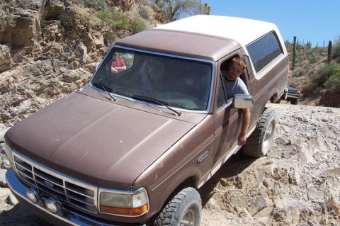 1993 Ford Bronco - A brown Ford Bronco navigates a challenging off-road path with a second vehicle visible behind it.