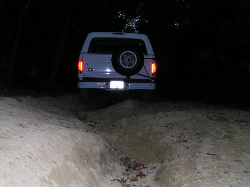 White 1996 Ford Bronco rear view on dirt trail at night