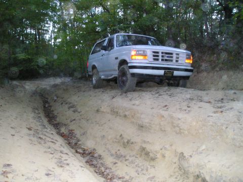 1996 Ford Bronco - A white SUV navigates a challenging dirt path, its front grille suggesting a model year around 1992.