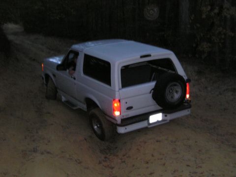 1996 Ford Bronco - A white Ford Bronco navigates a dirt path in low light conditions, with its spare tire visible on the rear.