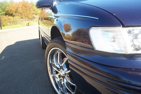 1993 Ford Taurus - A dark blue sedan is parked on asphalt, with trees and foliage visible in the background.