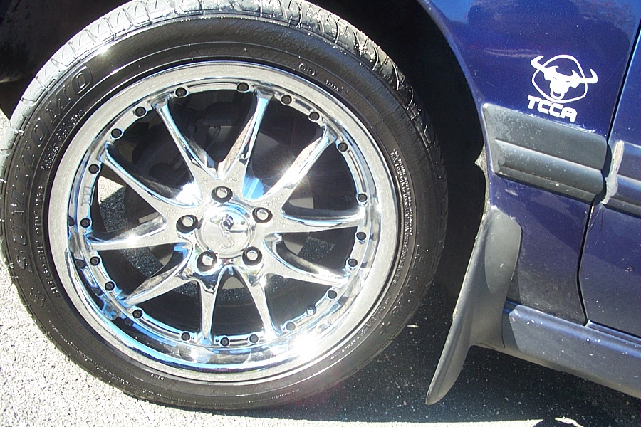 Chrome aftermarket wheel on a blue car with a TCCA logo on the fender