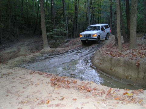 1996 Ford Bronco - A white 1996 Ford Bronco navigates a muddy path through a dense forest.