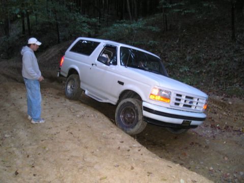 1996 Ford Bronco - A white Ford Bronco navigates a dirt path in a wooded area at dusk.