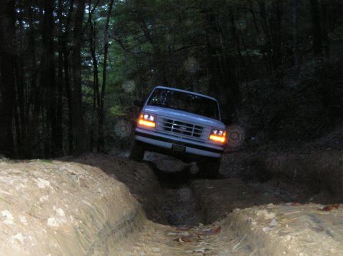 1996 Ford Bronco - White 1992 Ford Bronco tackles a challenging dirt trail, its headlights illuminating the path ahead.
