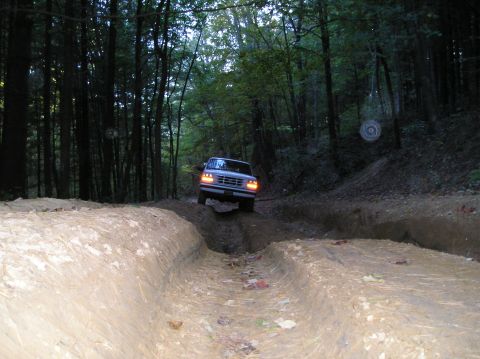 1996 Ford Bronco - Ford Bronco navigating a challenging muddy trail surrounded by dense trees.