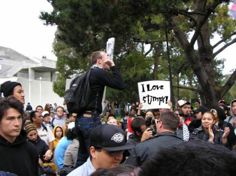 1994 Ford Crown Victoria - A man addresses a crowd while holding a rolled-up paper to his mouth, and someone in the crowd holds a sign.
