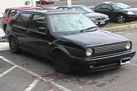 1996 Ford Bronco - A black Volkswagen Golf GTI is parked in a lot with other vehicles in the background.