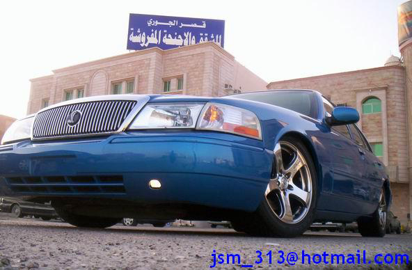 Low-angle front three-quarter view of a blue Mercury Grand Marquis on chrome aftermarket wheels