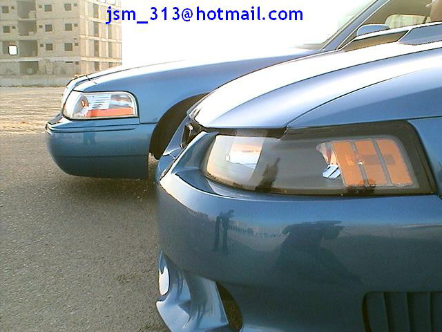 Front view of a blue Ford Mustang and a blue Mercury Grand Marquis parked on asphalt