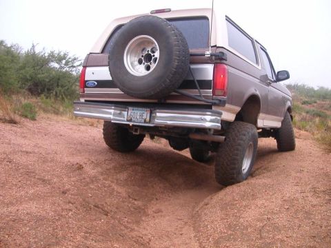 1993 Ford Bronco - Rear view of a 1993 Ford Bronco driving on a dirt trail with a spare tire mounted on the back.