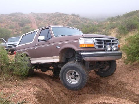 1993 Ford Bronco - This 1993 Ford Bronco is navigating a challenging off-road path with a second vehicle visible in the background.