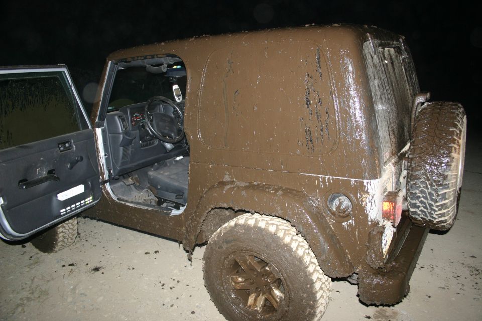 Mud-covered Jeep Wrangler at night, driver's door open, caked hardtop and mud-terrain tires