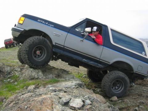 1989 Ford Bronco - A lifted Ford Bronco navigates a rocky trail, with another vehicle visible in the background.
