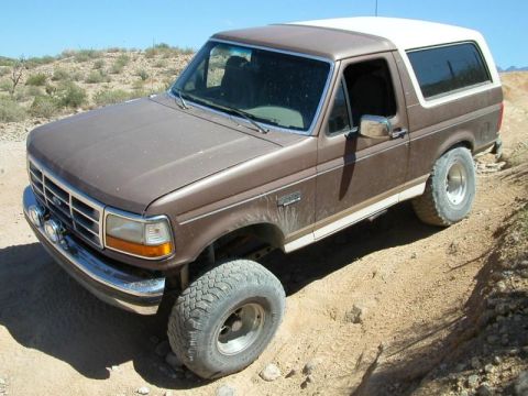 1993 Ford Bronco - This Ford Bronco is navigating a rough, dusty terrain under a clear blue sky.