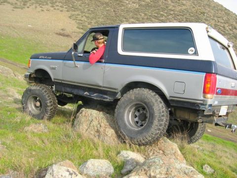 1989 Ford Bronco - This 1989 Ford Bronco is shown off-roading over rocks on a grassy hillside.