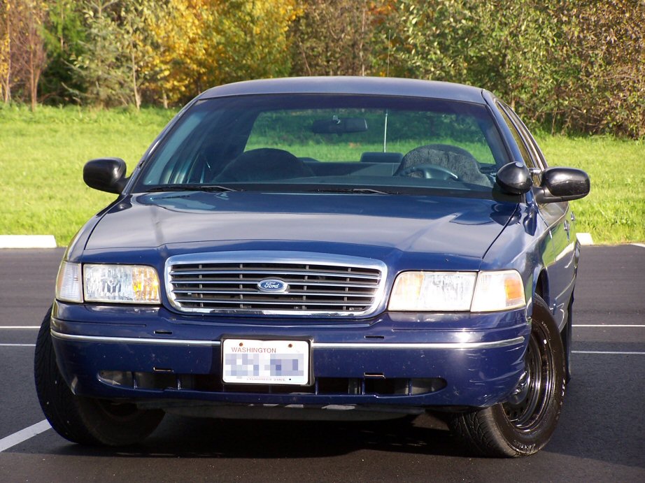 Front view of a blue Ford Crown Victoria parked outside with trees in the background