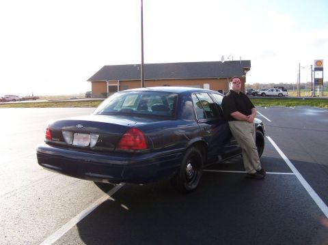 2001 Ford Crown Victoria - A man poses next to a dark blue 2001 Ford Crown Victoria, captured from the rear three-quarter angle.