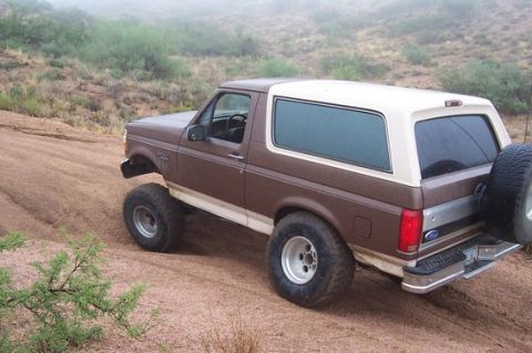 1993 Ford Bronco - This 1993 Ford Bronco is shown off-roading on a dusty trail with hills in the background.