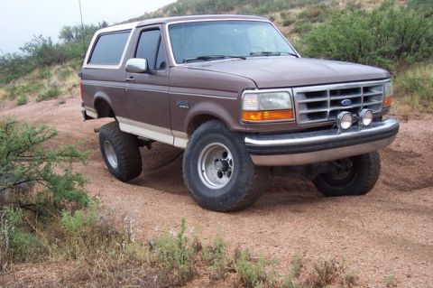 1993 Ford Bronco - This lifted 1993 Ford Bronco is shown in a 3/4 front view, parked on a dirt road with scrub brush.