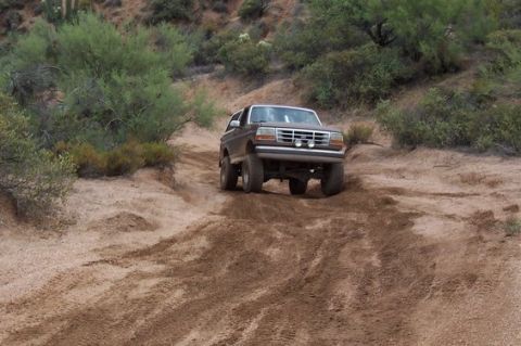 1993 Ford Bronco - Ford Bronco navigates a challenging off-road trail in a dry, arid landscape.