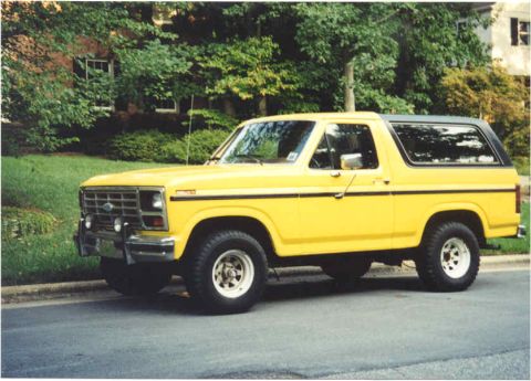 1985 Ford Bronco - A bright yellow 1985 Ford Bronco with a black removable top is shown from the side.