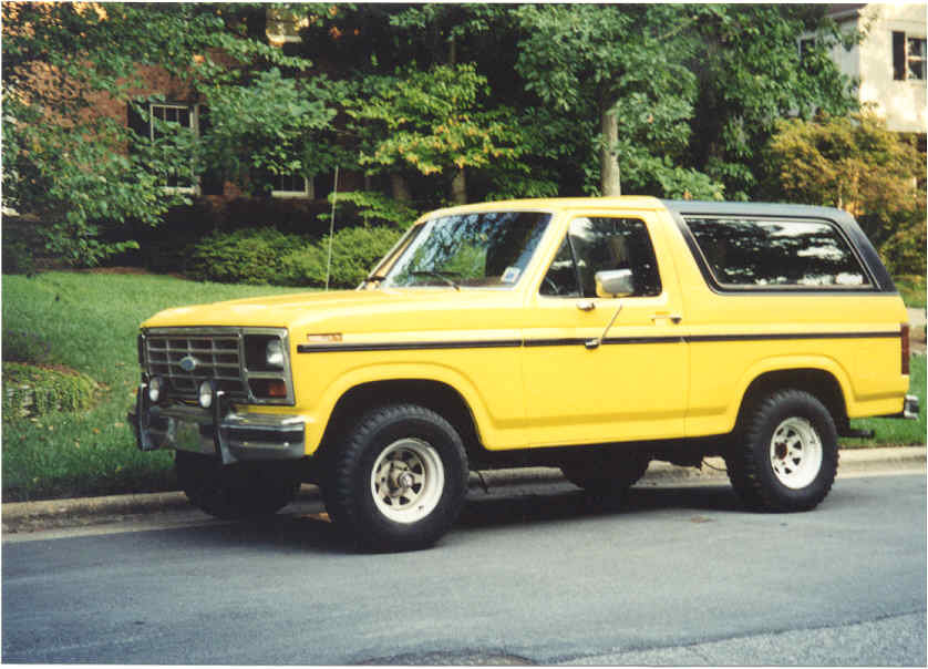 Yellow Ford Bronco with black top on white wheels parked at a suburban curb