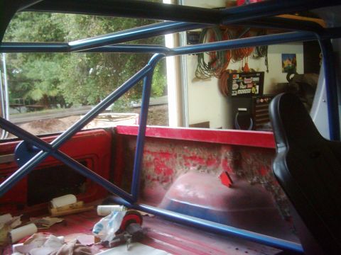 1978 Ford Bronco - Interior view of a truck bed with a custom blue roll cage and a black racing seat.