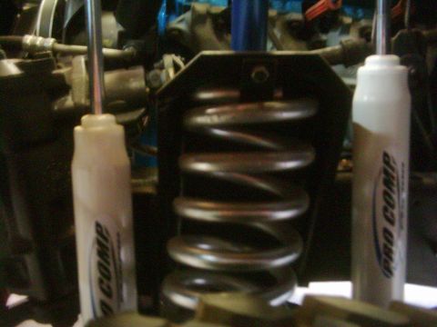1978 Ford Bronco - Tight underbody shot of a lifted 4x4 front suspension with a dark coil spring in its bracket flanked by a pair of white Pro Comp shock abso…