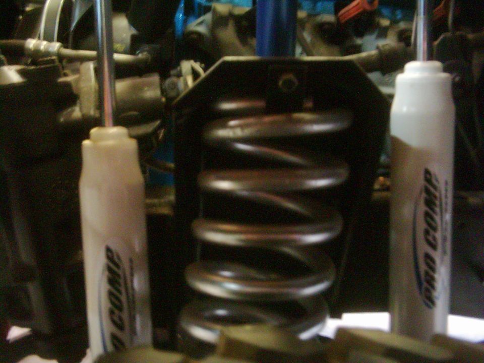 Coil spring flanked by two white Pro Comp shocks on lifted 4x4 front suspension