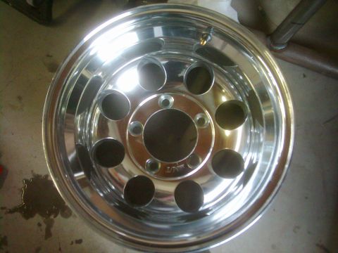 1978 Ford Bronco - A single chrome wheel is shown, a polished finish and eight distinctive circular openings around the central hub.
