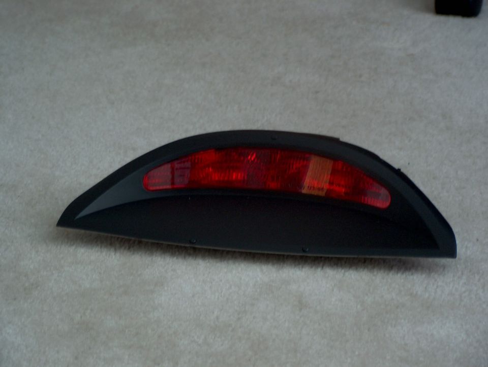 Black and red third brake light assembly with a curved black housing, resting on a carpeted surface