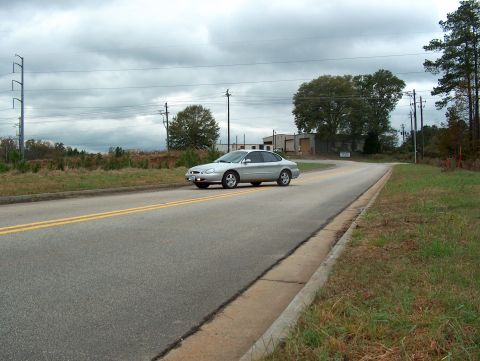 1998 Ford Taurus - A silver sedan drives down a road with industrial buildings in the background under a cloudy sky.