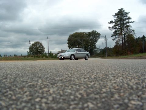 1998 Ford Taurus - Silver 1998 Ford Taurus seen from a low angle on a road under a cloudy sky.