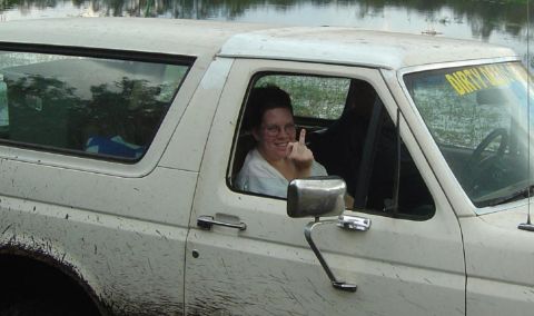 1993 Ford Bronco - A white SUV, likely from the 1980s, is shown covered in mud with its driver giving an offensive gesture.
