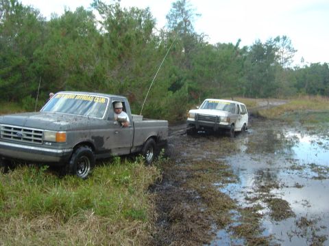 1993 Ford Bronco - A white 1992 Ford Bronco is stuck in the mud, with a gray pickup truck assisting it.