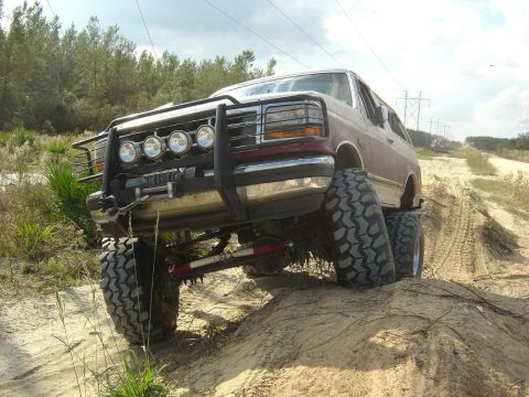 1993 Ford Bronco - Ford Bronco with aftermarket modifications navigating an off-road trail.