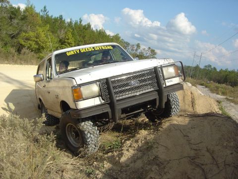 1993 Ford Bronco - This white Ford Bronco is navigating an off-road trail with a "Dirty Deeds Offroad" banner on the windshield.