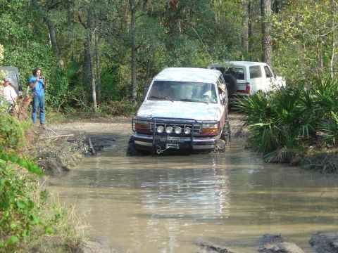 1993 Ford Bronco - This 1993 Ford Bronco is shown off-roading through a muddy water crossing, with another vehicle following closely behind.
